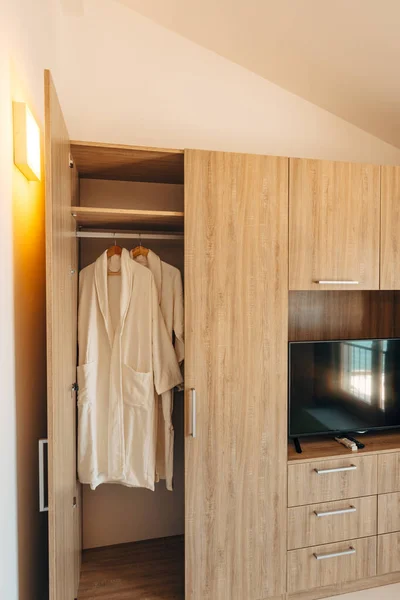 Dos túnicas blancas dentro de un armario con una puerta abierta y un nicho debajo de un televisor de plasma — Foto de Stock