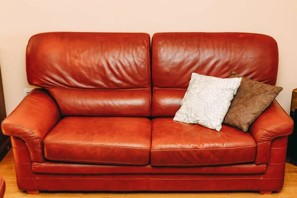 Раскладной диван из бордовой натуральной кожи с белыми и коричневыми подушками в номере. — стоковое фото