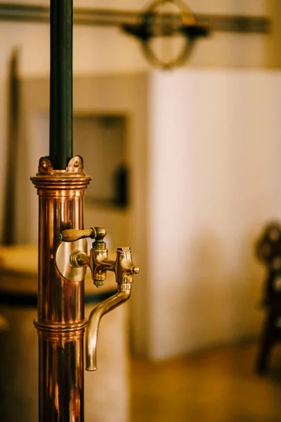 Uma torneira de cobre com uma alça de madeira em um recipiente com líquido em um fundo embaçado de uma cozinha de cor clara. — Fotografia de Stock