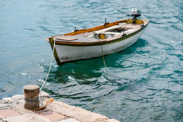 Une vieille borne maritime en pierre sur la jetée, avec un bateau de pêche en bois attaché. — Photo