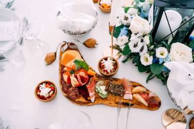 Masanın üzerinde dilimlenmiş jambon, sosis ve peynir ve bir buket salata ve bir buket çiçekle kesme tahtası..