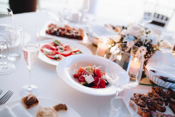 Platos con ensalada de verduras y bruschetta en una mesa festiva con un mantel blanco, vasos y velas. — Foto de Stock