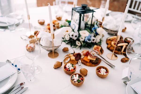 A festively decorated table with a white tablecloth, a candle in a candlestick in the center and delicacies on cutting boards. — Stock Photo, Image