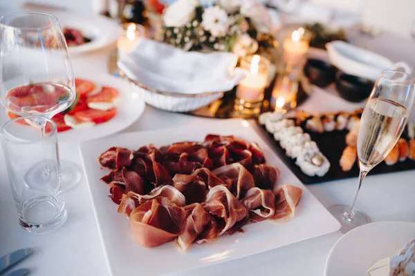 Primer plano de un plato blanco cuadrado con prosciutto en una mesa servida festivamente con juego de sushi y tomates en un mantel blanco. — Foto de Stock