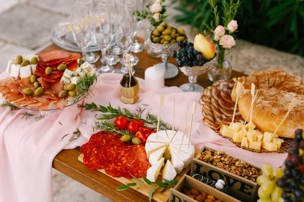 Sebuah meja dengan makanan lezat, buah-buahan dan kacang-kacangan. Wooden memotong papan dengan sosis chorizo, keju brie dan tomat. — Stok Foto