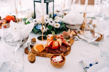 Kesik domates, sosis ve jambonla kesme tahtası kaseler, bardaklar ve çiçeklerle dolu bir masada..
