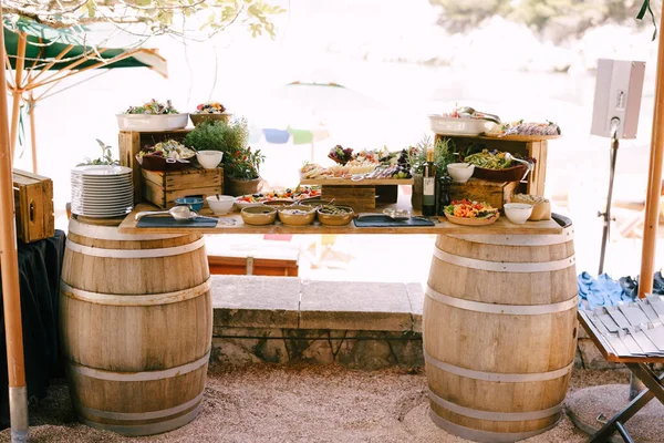 Improvizovaný stůl se dvěma sudy vína a dřevěným barem s lahůdkami a květinami. — Stock fotografie