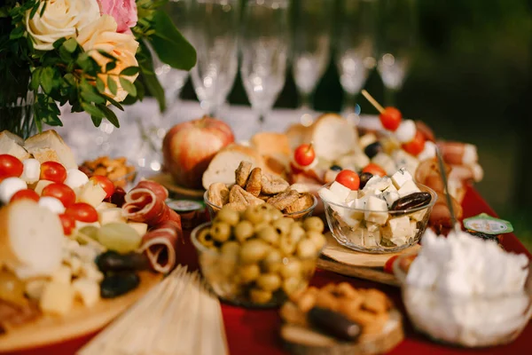 Mesa con mantel de paño rojo, servida para el evento con aceitunas, queso y embutidos, higos secos y copas de champán vacías. — Foto de Stock