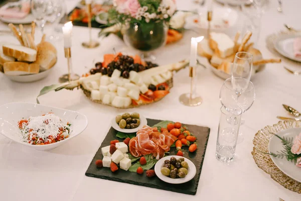 El jamón, las aceitunas grandes verdes sobre los platillos, el queso y las fresas y las frambuesas sobre la tabla de cortar de madera sobre la mesa de fiesta. — Foto de Stock