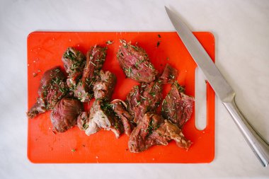 Kırmızı bir kesme tahtasında büyük bir bıçakla kesilmiş çiğ biftek..