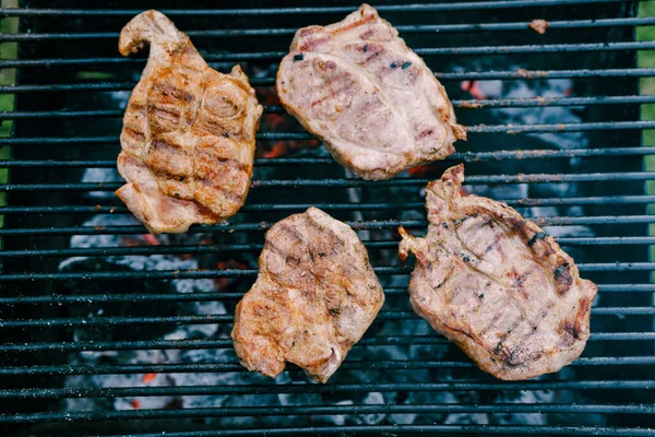 Four flat pieces of steak on a metal grill, fried on hot coals. — Stock Photo, Image