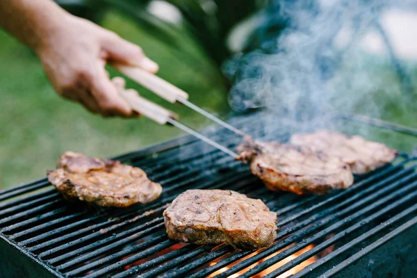 The chef flips the meat on a metal grille with smoke and fire with tongs. — Stock Photo, Image
