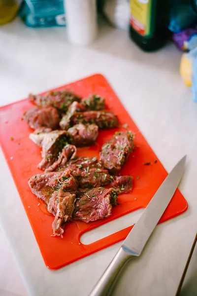 Kırmızı bir kesme tahtasında büyük bir bıçakla kesilmiş çiğ biftek..