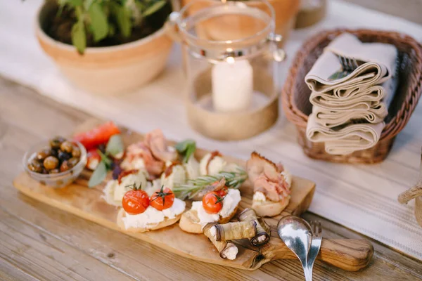 Деревянная доска для резки холодными нарезками, хлебом и оливками на размытом фоне праздничного стола. — стоковое фото