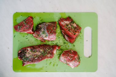 Yeşil bir kesme tahtasına çiğ biftek parçaları serpilmiş tuz ve biberiye serpiştirilmiş, ayçiçeği yağı dökülmüş..