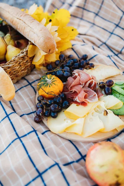 Plato con radómero de queso duro, jamón y uvas en una cama con baguette fresca y hojas amarillas. —  Fotos de Stock