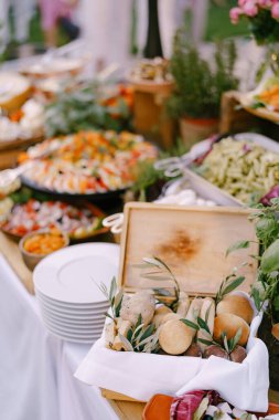 Masada ekmek sepeti, salatalar, temiz tabaklar ve bulanık arka plandaki saksılarda çiçekler..