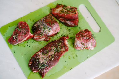 Yeşil bir kesme tahtasına çiğ biftek parçaları serpilmiş tuz ve biberiye serpiştirilmiş, ayçiçeği yağı dökülmüş..