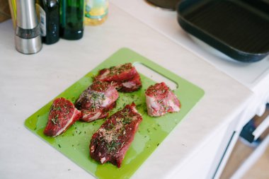 Yeşil bir kesme tahtasına çiğ biftek parçaları serpilmiş tuz ve biberiye serpiştirilmiş, ayçiçeği yağı dökülmüş..