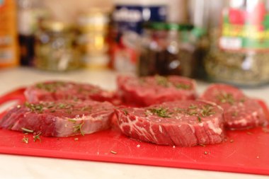 Kırmızı bir kesme tahtasına beş çiğ et parçası serpiştirilmiş biberiye ve kaba tuz..