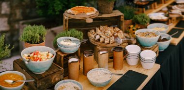 Bakır bardaklar, yemek tabakları, pizza ve hamur işleri mutfak gereçleriyle dolu uzun bir masada. Restoranda kahvaltı için büfe masası..