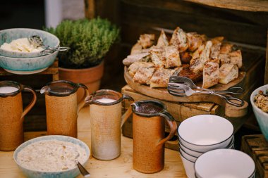 Sütlü ve sıcak çikolatalı bakır bardaklar, sütlü yulaf lapası ve taze hamur işleriyle dolu tabağın yanında..