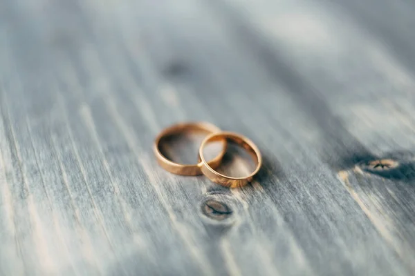 Detailní záběr na zlaté snubní prsteny na šedé dřevěné textuře na rozmazaném pozadí. — Stock fotografie