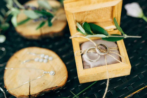 Open houten doos met trouwringen en een houten standaard met oorbellen en een ketting met een hanger. — Stockfoto