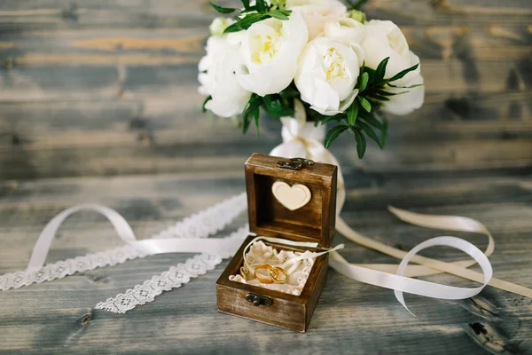Caja de madera con dos anillos de boda sobre un fondo gris con un ramo de peonías blancas. —  Fotos de Stock