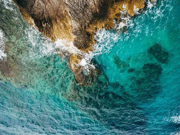 Azul azur agua de mar, olas blancas espumosas golpeando la costa rocosa, vista aérea. — Foto de Stock