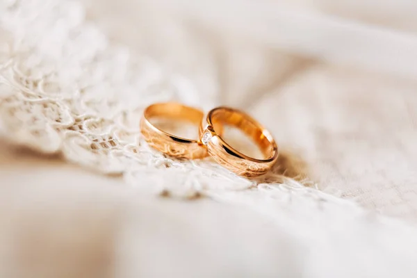 Két arany jegygyűrű a menyasszonynak és a vőlegénynek, ékkövekkel a fehér csipkén.. — Stock Fotó