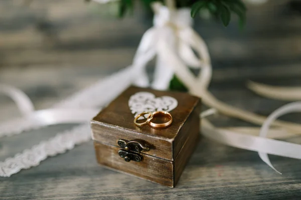 Caja de madera cerrada con un corazón y anillos de oro para la novia y el novio sobre un fondo de cintas blancas. —  Fotos de Stock