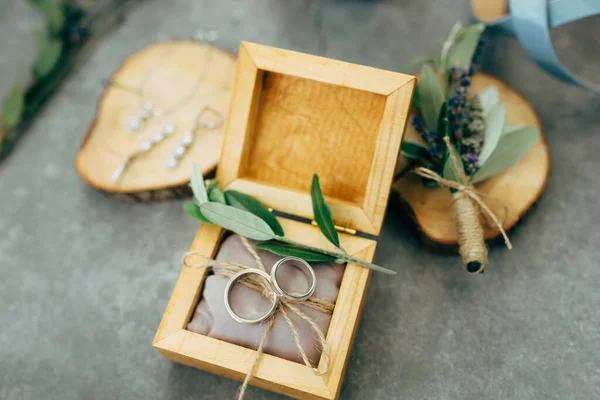 Een open houten doos met trouwringen en houten standaards met sieraden en een boeket bloemen. — Stockfoto