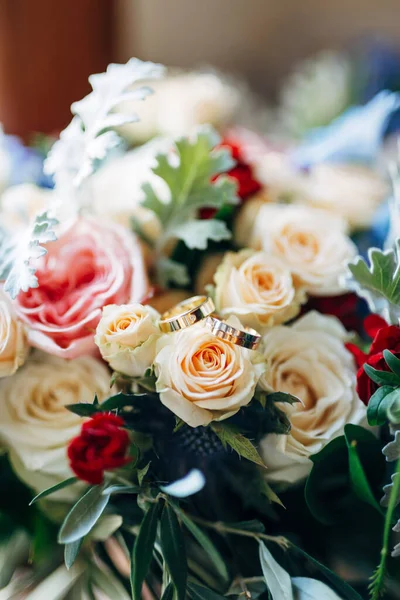 Anéis de casamento de ouro em um botão em um buquê de rosas vermelhas e brancas. — Fotografia de Stock