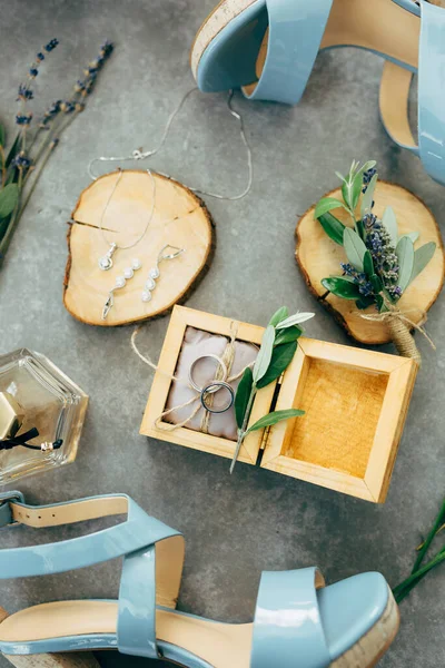 Una caja de madera abierta con anillos de boda sobre un fondo gris y zapatos de dama de honor azules. —  Fotos de Stock