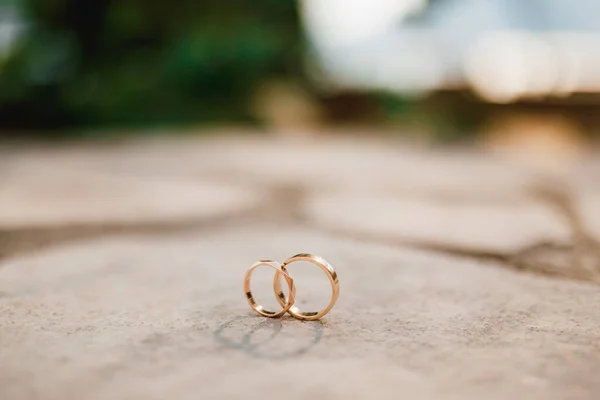 Arany gyűrűk egy esküvő függőleges helyzetben, homályos háttér. — Stock Fotó