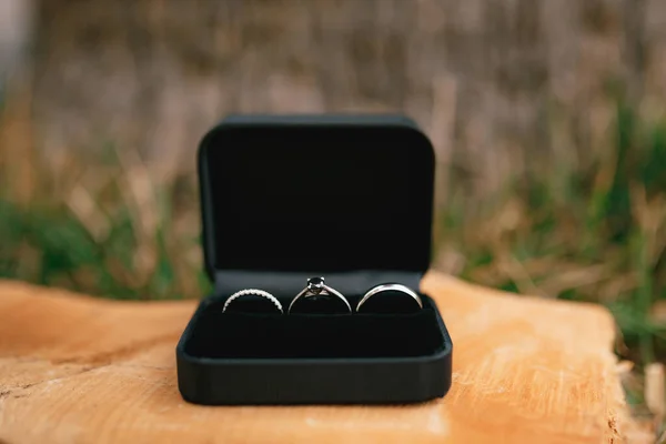 Anéis de casamento em ouro branco e um anel de noivado em uma caixa de veludo preto em uma base de madeira. — Fotografia de Stock