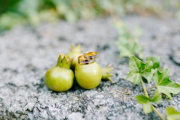 Anillos de boda de oro en pequeños frutos de granada sobre un fondo borroso. —  Fotos de Stock