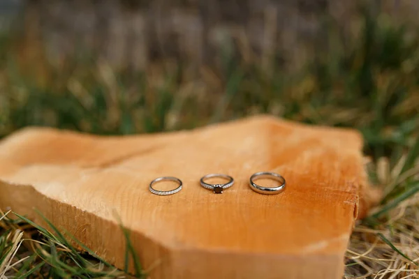 Anéis de casamento de ouro e um anel de noivado em um corte de madeira suave na grama. — Fotografia de Stock