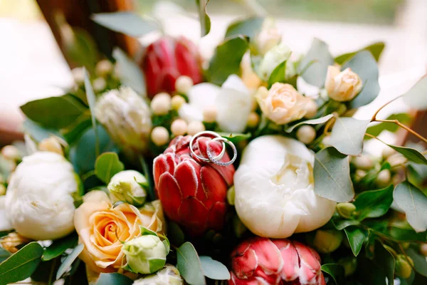 Anéis de casamento da noiva e noivo em um botão em um buquê de rosas e peônias em vermelho e branco. — Fotografia de Stock