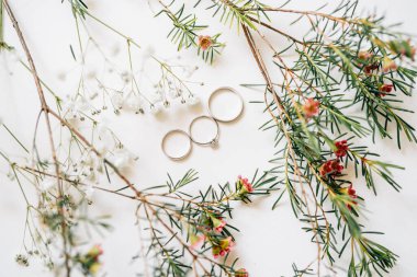 Gelin ve damat için iki alyans ve çiçeklerle süslü beyaz bir arka planda gelin nişan yüzüğü..