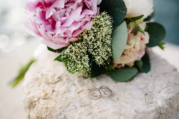 Gold wedding rings in white gold and an engagement ring on a white background with a bouquet of peonies.