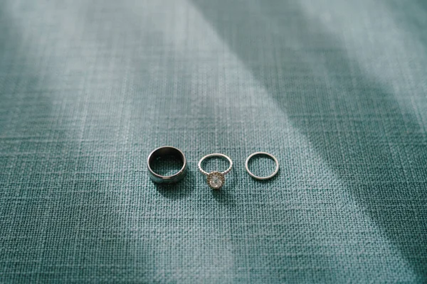 Anéis de casamento da noiva e do noivo e o anel de noivado da noiva com uma pedra preciosa em um tecido cinza denso. — Fotografia de Stock