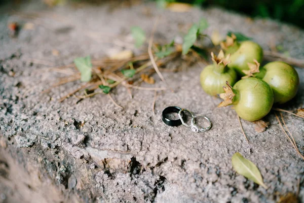 Nevěsty zásnubní prsten a nevěsta a ženich prsteny na kamenné textuře s malým granátovým jablkem ovoce. — Stock fotografie