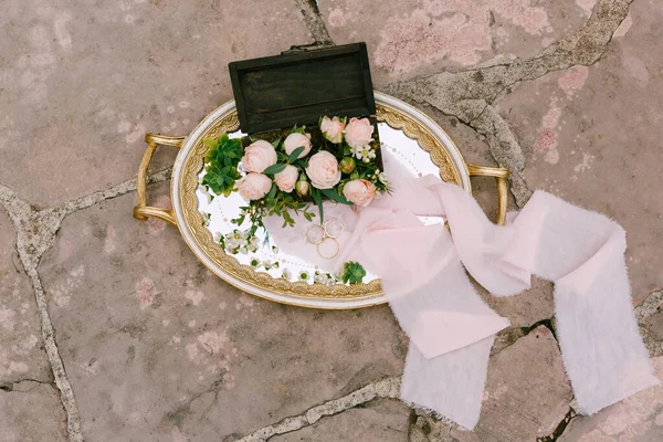 Anillos de boda y un anillo de compromiso en una bandeja con motivos y un ramo de rosas rosadas en una caja de madera. —  Fotos de Stock