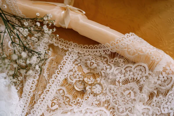 Anéis de casamento e um anel de noivado vestido de casamento branco da noiva com rendas e flores silvestres em uma mesa de madeira. — Fotografia de Stock