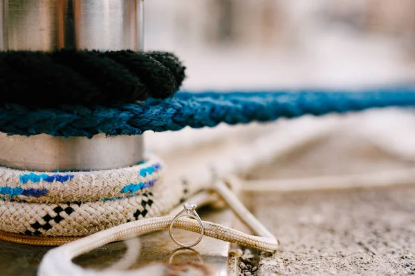 The brides engagement ring with a precious stone on the ground by a steel pipe with ropes.