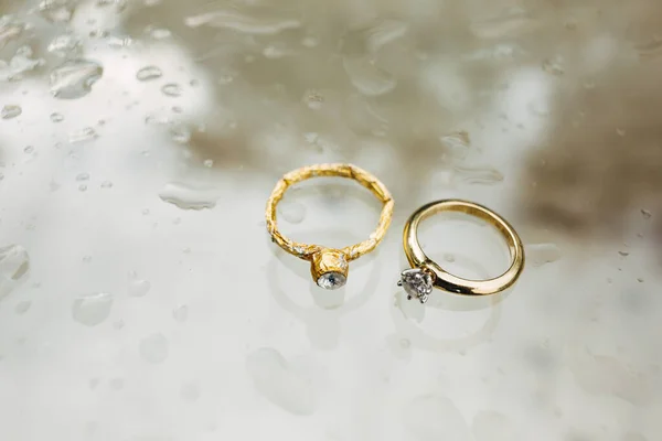 Anel de noivado de noivas e anel de folha em um fundo branco fosco em gotas de água. — Fotografia de Stock