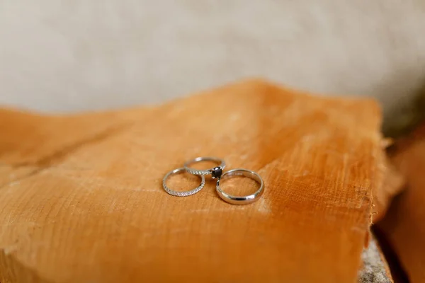 Anéis de casamento de ouro e anel de noivado no fundo borrado de textura de madeira lisa. — Fotografia de Stock