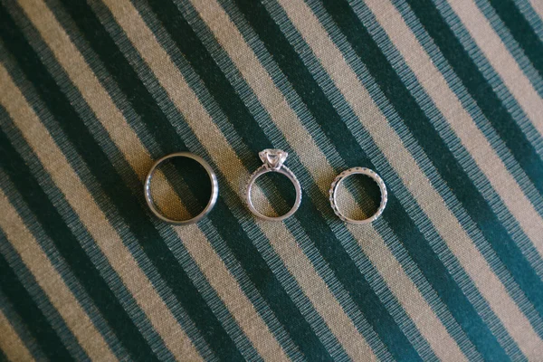 Close-up de anéis de casamento de ouro branco e um anel de noivado de pedra preciosa para uma noiva em tecido azul com listras brancas. — Fotografia de Stock